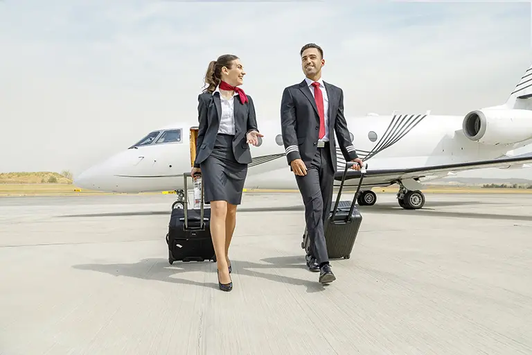A Jetwise flight crew walks confidently on the tarmac, dressed in professional uniforms with rolling suitcases in hand. Behind them, a luxury private jet awaits its next departure, representing Jetwise's elite aviation services.